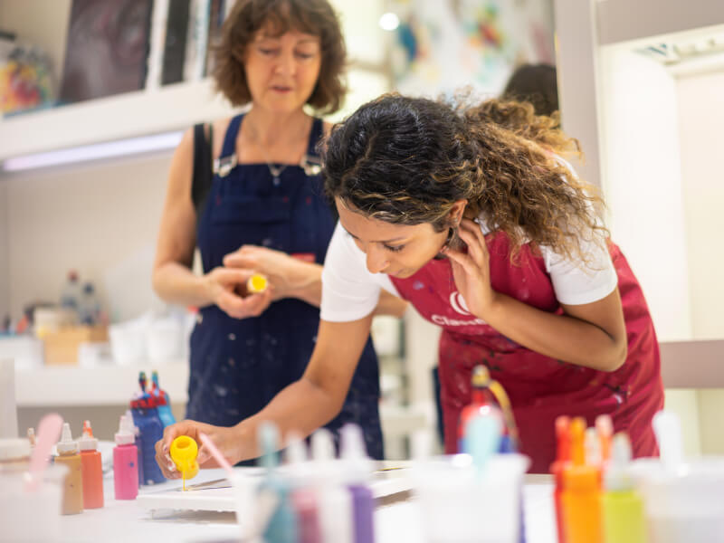 A student pouring yellow paint on to a canvas as the teacher observes